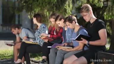 侧面不同的大学生坐在公园的长凳上<strong>阅读书籍</strong>和教科书，同时一起学习